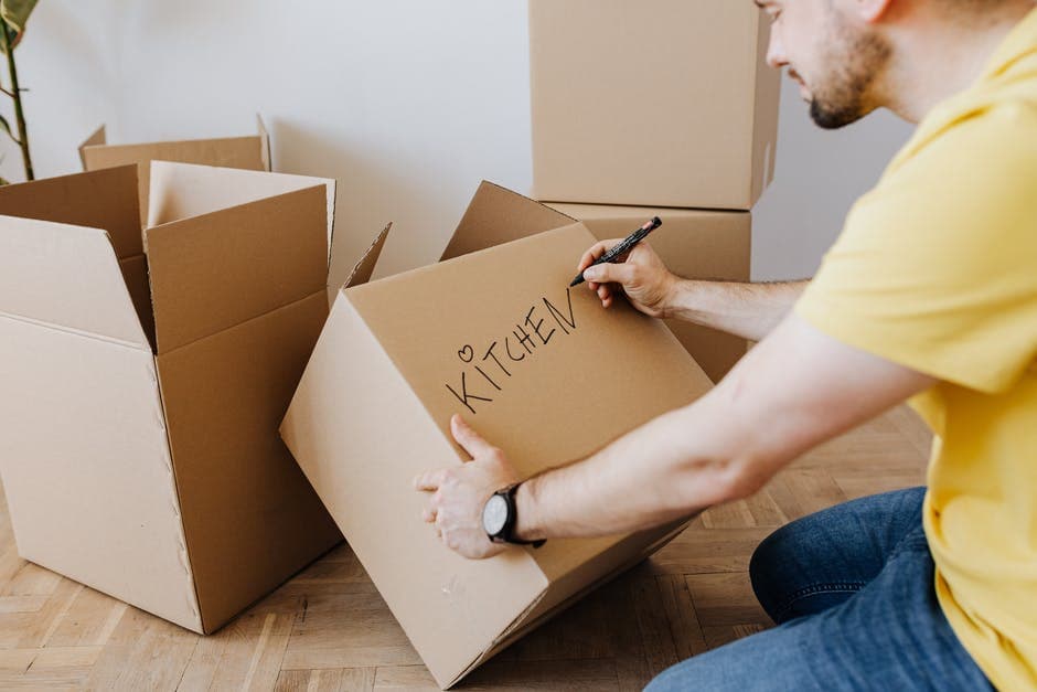 Man labeling moving boxes for kitchen items during packing process