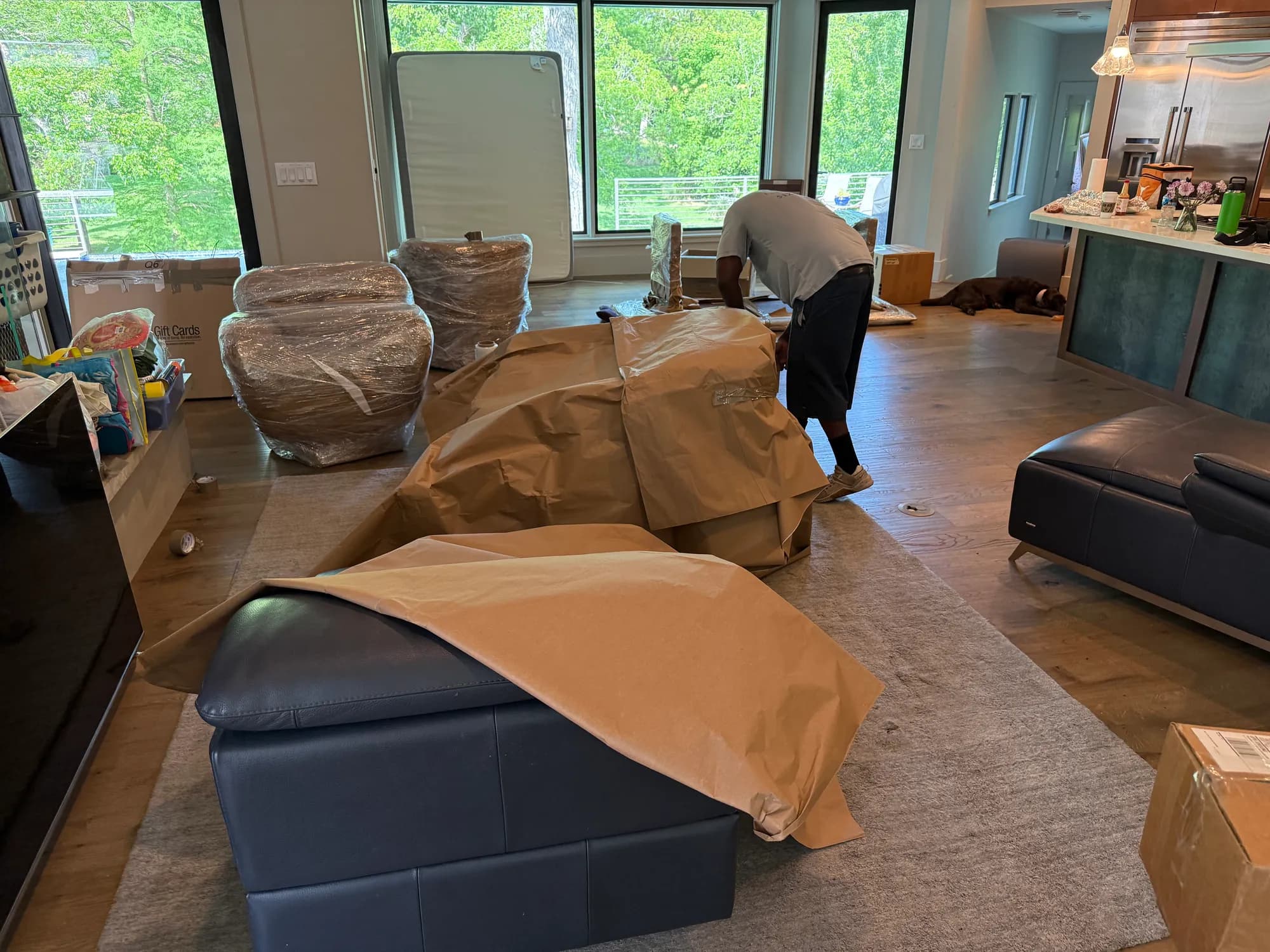 Muscleman Elite mover paper-wrapping fine furniture amid blanket-wrapped pieces