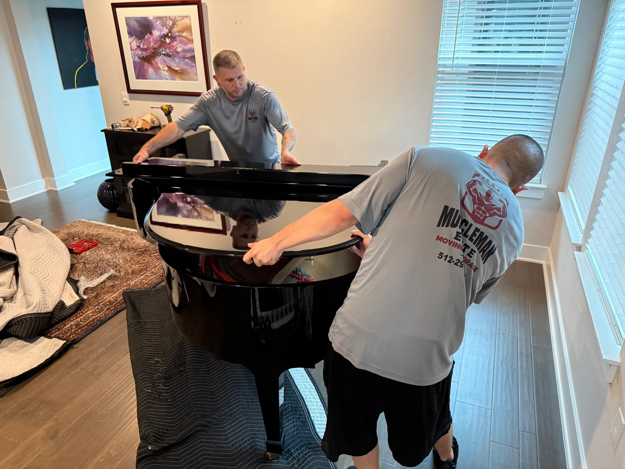 Muscleman Elite crew lifting a glossy black baby grand onto its side board