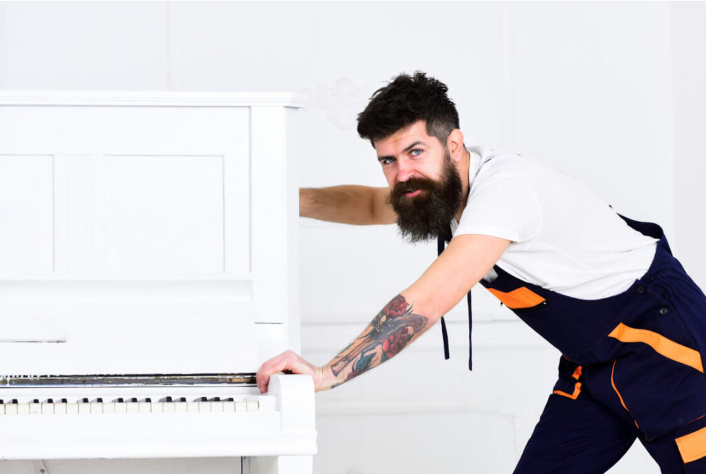 Mover pushing a white upright piano.